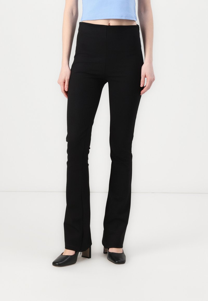 Black flared trousers with a smooth texture, high-waisted design, and a sleek silhouette, paired with black heeled shoes.
