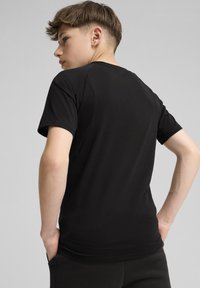 Melna īsām piedurknēm t-krekls ar gludu tekstūru, ar vienkāršu dizainu un pieguļošu formu, redzams no aizmugures uz neitrāla fona.