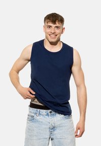 Canottiera in cotone senza maniche di colore blu navy con scollatura rotonda, indossata sopra dei pantaloni corti in denim azzurro, che rivelano una cintura nera sottostante.