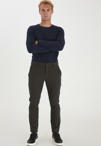 Mørkegrå bukser med en struktureret overflade, lige snit og sidelommer, parret med en tætsiddende marineblå langærmet skjorte og sorte sneakers.