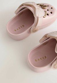 Roosa kummist klotsid tekstureeritud sisetallaga ja dekoratiivse nööbiga rihmal, millel on kuldne "BAKER" bränding ja ventilatsiooniaugud.