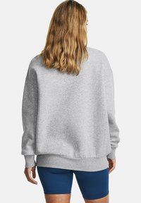 Grijze oversized sweatshirt met lange mouwen, geribbelde manchetten en een gebande rand, gecombineerd met blauwe sportshorts. Zachte katoenmix textuur.