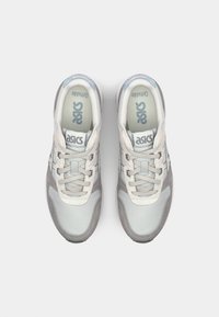 Light gray sneaker with mesh upper, round toe, and laces. Features silver accents and logo on tongue. Cushioned sole for comfort.