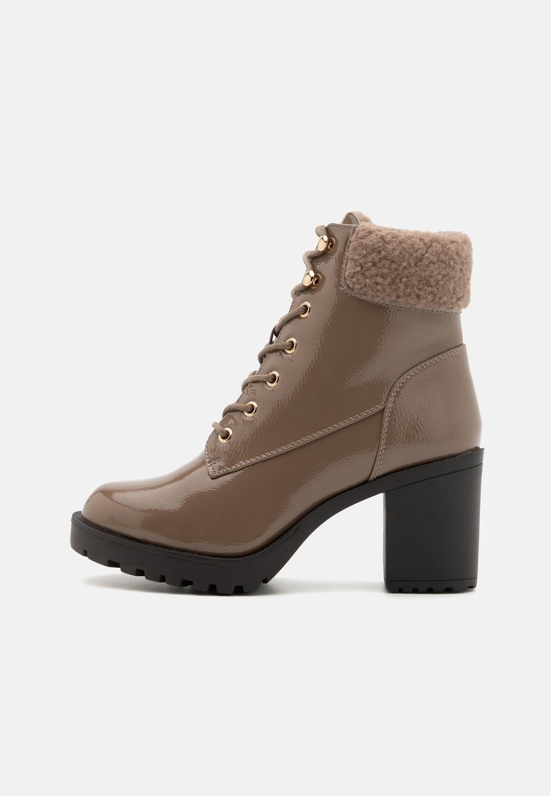 Bottine à talon haut en taupe brillant avec laçage sur le devant, œillets dorés, semelle noire épaisse et doublure moelleuse avec revers plié.