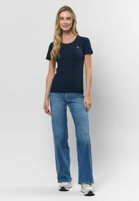 Námornícky pruhovaný krátky rukáv tričko s okrúhlym výstrihom a malým emblémom. V skombinovaní s svetlomodrými rozšírenými džínsy a bielymi športovými topánkami.