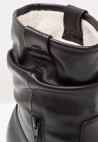 Botte en cuir noire avec fermeture éclair latérale et doublure intérieure en polaire blanche douce au niveau du revers.