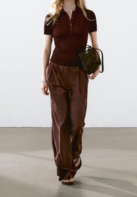 Burgundy ribbad polo skjorta med korta ärmar, parat med vida, mörk burgundy byxor och en liten svart mocka handväska. Platta sandaler.