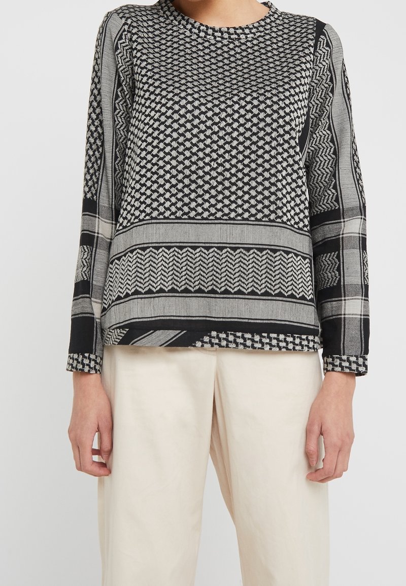 Haut à manches longues à motifs noirs et gris avec des designs géométriques, col rond et coupe droite ; associé à un pantalon beige clair.