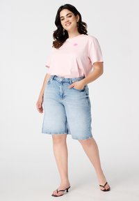 T-shirt rose avec un graphisme de coquillage, associé à un short en denim bleu clair. La tenue présente une coupe décontractée et une texture de tissu lisse.