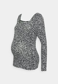 Camisola de maternidade de mangas longas feita de um tecido elástico preto com bolinhas brancas irregulares, apresentando um decote em bico e uma forma ajustada.