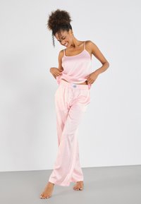 Rosa satin camisole med tynne stropper, parret med lyserosa pyjamasbukser med et subtilt leopardmønster og elastisk midje.