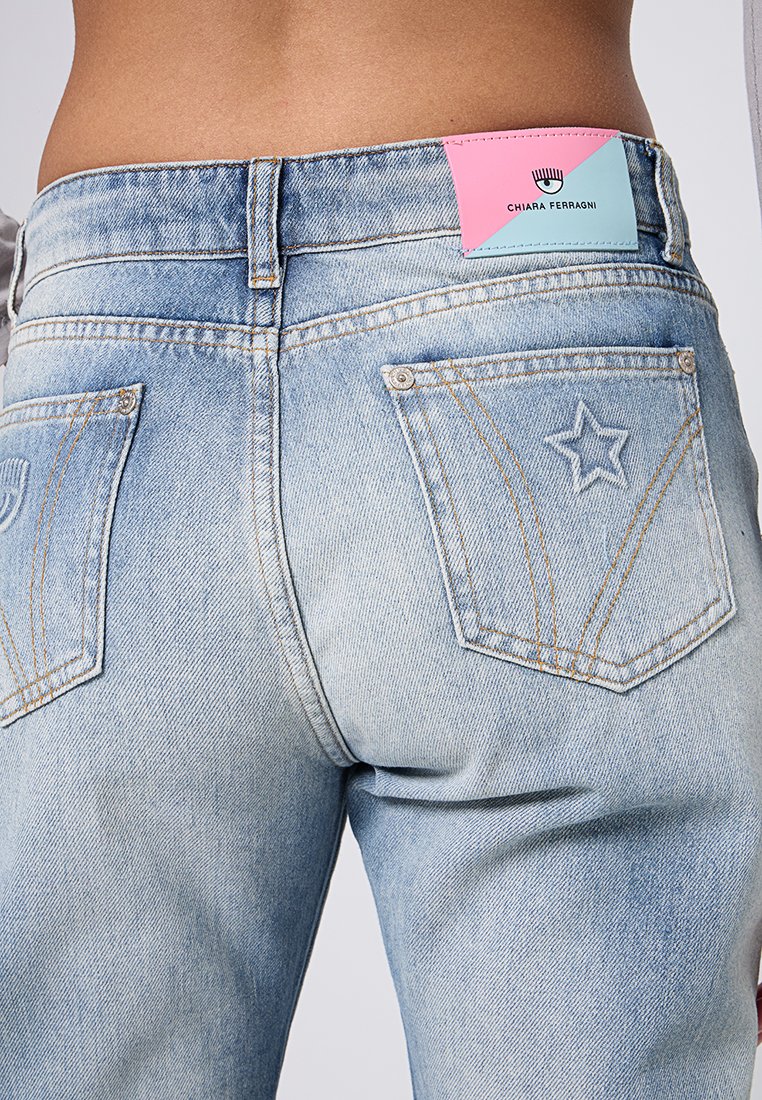 Los vaqueros de mezclilla azul claro presentan una cintura alta, costuras en contraste y un diseño de estrella en el bolsillo trasero, con una etiqueta colorida en la cintura.