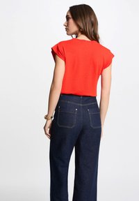 Rode T-shirt met korte mouwen en een ronde hals, gecombineerd met donkerblauwe wijde jeans met achterzakken en gele stikdetails.