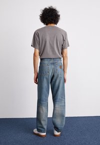 Grå kortärmad t-shirt i kombination med löst sittande, urblekta blå jeans. Jeansen har bakfickor och en läderlapp på midjebandet.