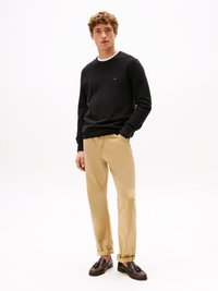 Pull noir en maille à col blanc, associé à un pantalon beige et des chaussures noires à enfiler. Coupe décontractée, design sobre.