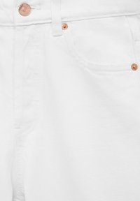 Gros plan sur un jean en denim blanc montrant la poche avant, la ceinture avec passant pour ceinture et les détails des rivets en cuivre.