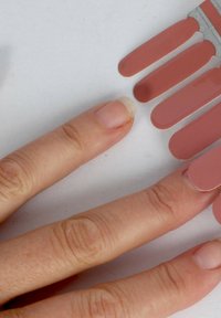 Nagellackfarbproben in unterschiedlichen Nude- und Rosatönen, fächerartig angeordnet neben einer Hand mit kurzen, natürlichen Nägeln.