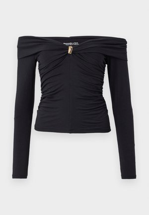 Sort off-shoulder langærmet top med sammensamlet struktur, der har en central drejning og guldtonet detaljer. Blødt strækstof.