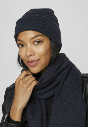 Merinovihreä neulepipo, joka on yhdistetty pitkään, tekstuuriseen huiviin samassa värissä. Pehmeä kangas, tiukasti istuva muotoilu, vähäisiä koristeita.