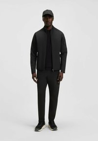 Czarna kurtka zapinana na suwak z wysokim kołnierzem, w połączeniu z czarną koszulką i dopasowanymi spodniami. Uzupełniona czarną czapką i czarnymi sneakersami.