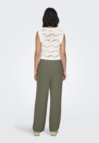 Haut blanc en crochet avec bords festonnés, associé à un pantalon large couleur vert olive, tous deux en tissu léger. Chaussures espadrilles naturelles.