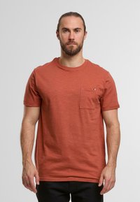 Rdzawoczerwony t-shirt z krótkim rękawem wykonany z miękkiego, teksturowanego materiału, z kieszenią na piersi i subtelnym akcentem logo.