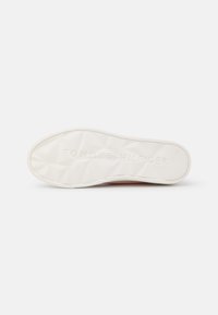 Semelle de chaussure en caoutchouc blanc avec un motif géométrique texturé. Présente le logo de la marque "TOMMY HILFIGER" embossé le long du bord.