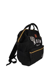 Sac à dos en denim noir avec une poche zippée à l'avant, des accents de fermeture éclair jaune, des patchs de logo et un emblème rond. Comprend deux bretelles ajustables.