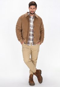 Brun kordfløjljakke med knaplukning, ternet skjorte under, beige cargo bukser og brune ruskind støvler med kraftige såler.