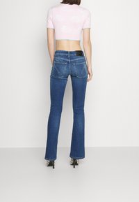 Jeans de campana azul con un ajuste de cintura media. Cuenta con dos bolsillos traseros, presillas para el cinturón y una etiqueta de cuero negro en la cinturilla.