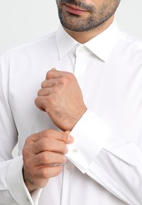 Wit overhemd met klassiek kraag, knoopsluitingen en lange mouwen. De stof oogt glad met een frisse textuur.