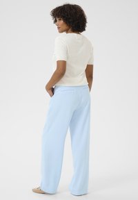 Light cream short-sleeve top with textured accents, paired with high-waisted, loose-fitting light blue trousers. Textured fabric visible.