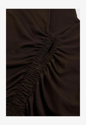 Detailní záběr tmavé látky se nařaseným šitím, které vytváří texturované záhyby a středový šev.