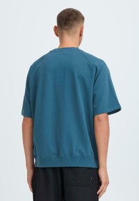 Zilā krāsa crewneck džemperis ar īsām raglan piedurknēm, mīksta tekstūra un ribota apkakle un apakša, kombinēts ar melnām biksēm.