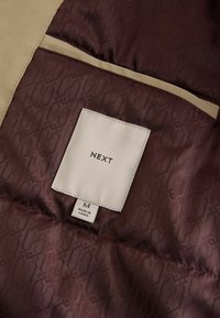 Burgundy-interiorkangas, jossa on sävykuvio, vaaleanbeige kangasreunus. Mukana ommeltu etiketti, jossa on brändin nimi ja kokotiedot.