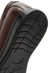 Chaussure en cuir brun avec une semelle en caoutchouc noir présentant un motif de bande de roulement pour une meilleure adhérence, mettant en avant la durabilité et le design anti-dérapant.