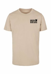 Beige bomulds T-shirt med et sort grafisk tekstdesign med "MEIN ♥ SCHLÄGT SCHLAGER" på den øverste venstre brystområde. Klassisk rund hals.