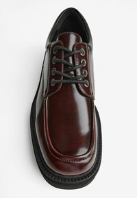 Scarpa stringata in pelle bordeaux con finitura lucida, punta tonda, suola in gomma e accenti neri a contrasto sul tallone e sui lacci.
