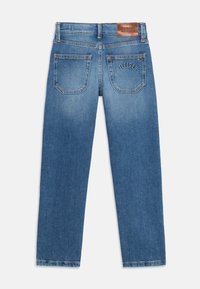 Jeans de denim azul claro com corte reto, apresentando dois bolsos traseiros e uma etiqueta de couro castanho rotulada "TOMMY HILFIGER". Textura suave.