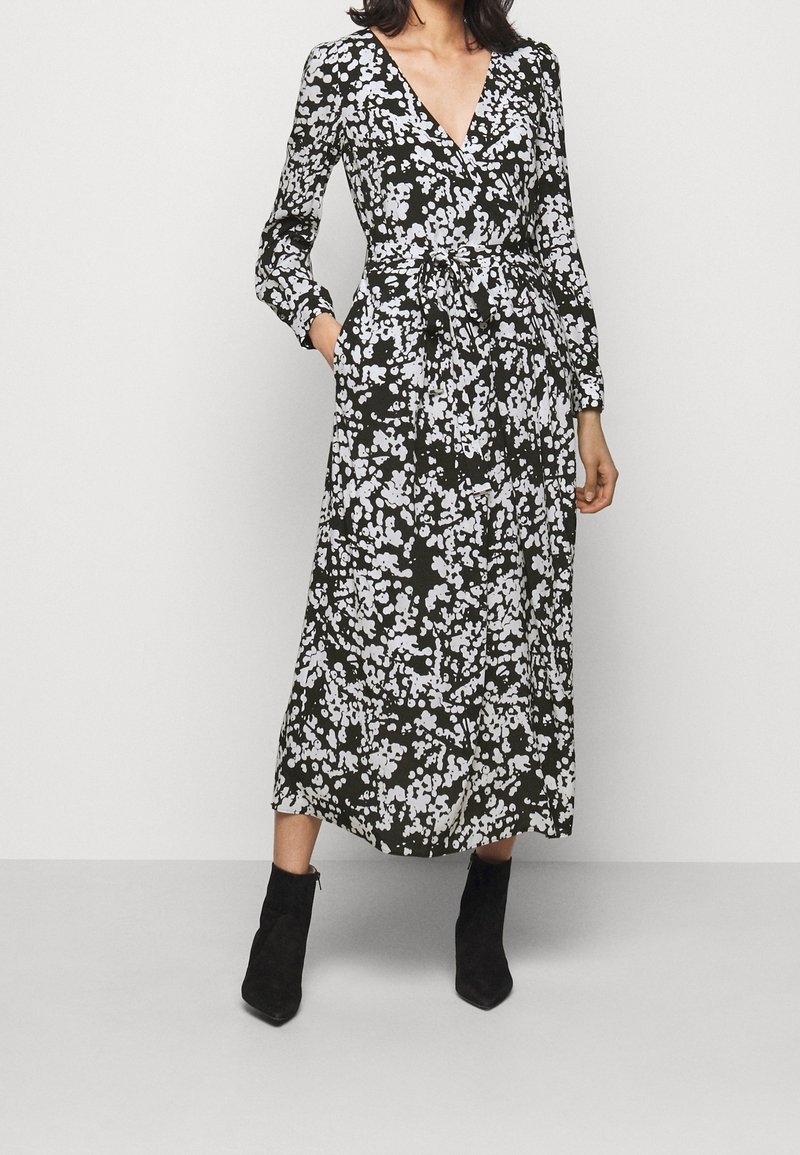 Musta, kukkakuvioinen kietaisumekko, jossa pitkät hihat, V-pääntie, sidottava vyötärö ja puolipitkä helma, jossa valkoiset kukkakuviot. Yhdistetty mustiin nilkkureihin.