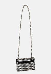 Borsa in bianco e nero con motivo a pois, realizzata in materiale testurizzato. Presenta una tracolla a catena argentata e una chiusura con patta piegata.