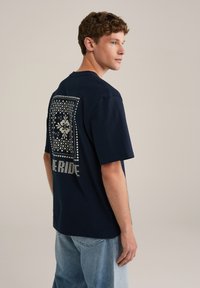 Sötétkék pamut póló rövid ujjakkal, nagyméretű nyomtatott mintával a háton, virágos és geometrikus mintákkal.