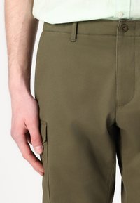 Olajzöld cargo nadrág sima, texturált felülettel, oldalzsebbel és elülső gombos záródással. A gomb és a varrás részletei láthatók.