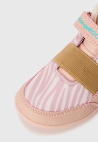 Rosa barnesko med zebra-mønster, med en tan elastisk stropp og en imitert skinn tåhette. KangaROOS-logo i turkis.