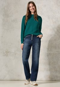 Teal ribbad tröja med rund halsringning, kombinerad med högmidjade mörk denimjeans med fem knappar, bärs med ljusa sneakers.