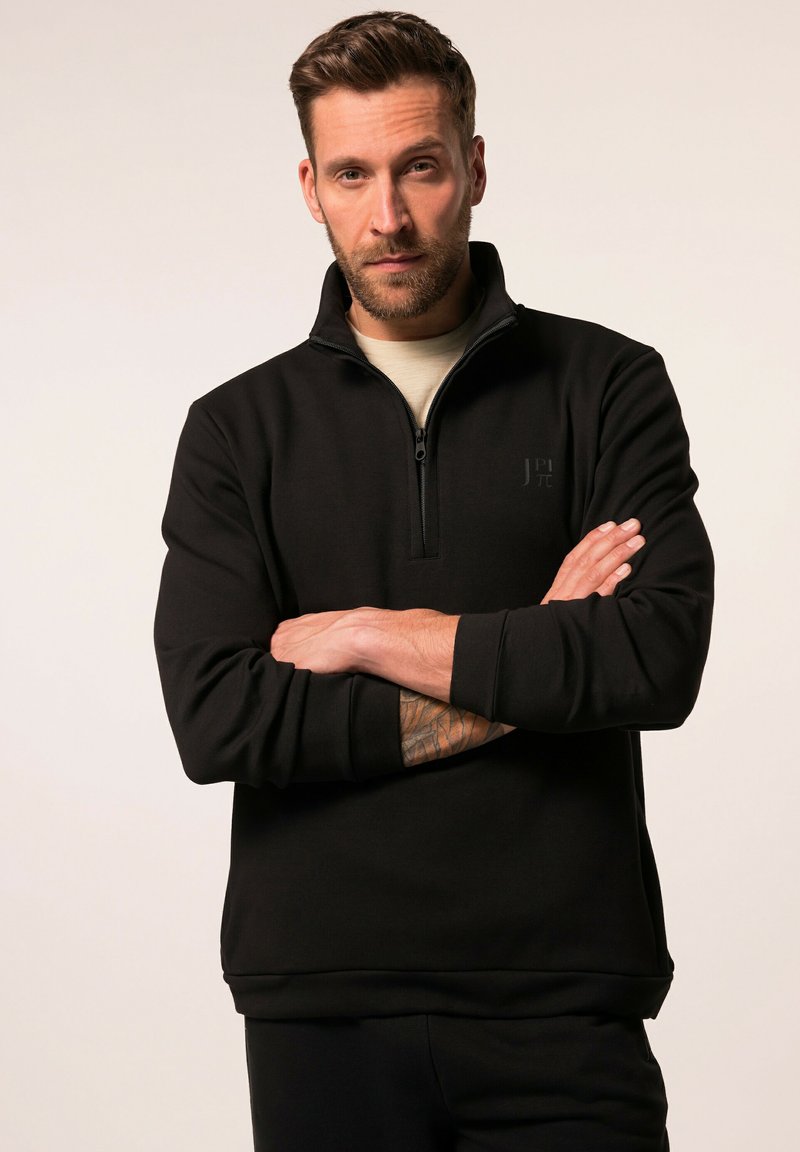Sudadera de forro polar negra con cremallera de cuarto, que presenta un cuello alto, dobladillo recto y un sutil logotipo en el pecho. Textura suave.