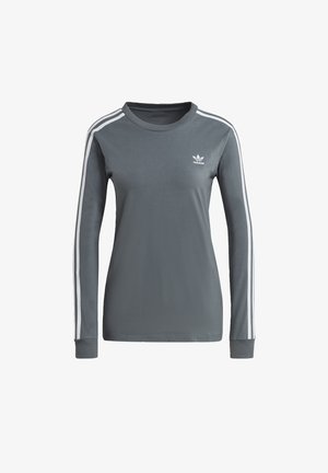 Grijs sportshirt met witte strepen, grijs geruit colbert en grijze spijkerbroek. Witte sneakers met zwarte strepen en bijpassende gestreepte sokken.