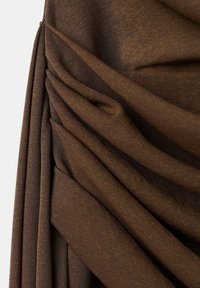 Tissu marron avec des plis superposés et torsadés et une texture douce, formant des plis diagonaux sur un fond clair.