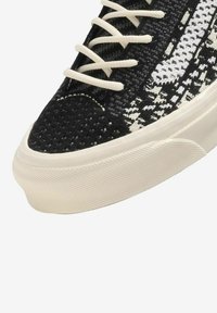 Sneaker a maglia bianca e nera con una tomaia testurizzata, dotata di lacci bianchi e suola in gomma con una finitura liscia e dettagli in rilievo.