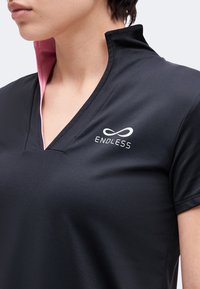 Personne portant une chemise noire avec un col intérieur rose et un logo blanc "ENDLESS" sur la poitrine gauche avec un symbole d'infini au-dessus.